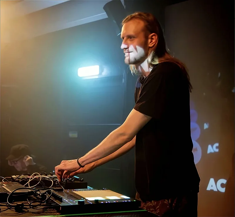 Accina playing a live set on hardware, lit by warm and blue stage lights
