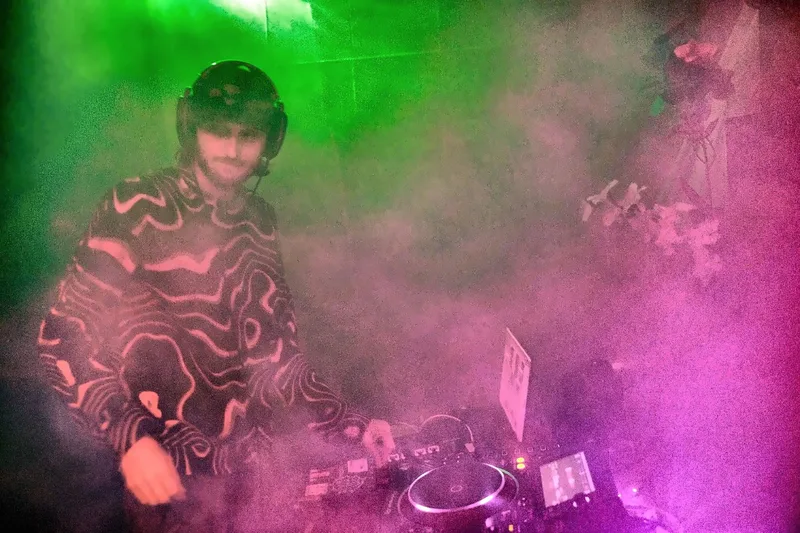 Accina at the decks in thick green and pink smoke, wearing headphones